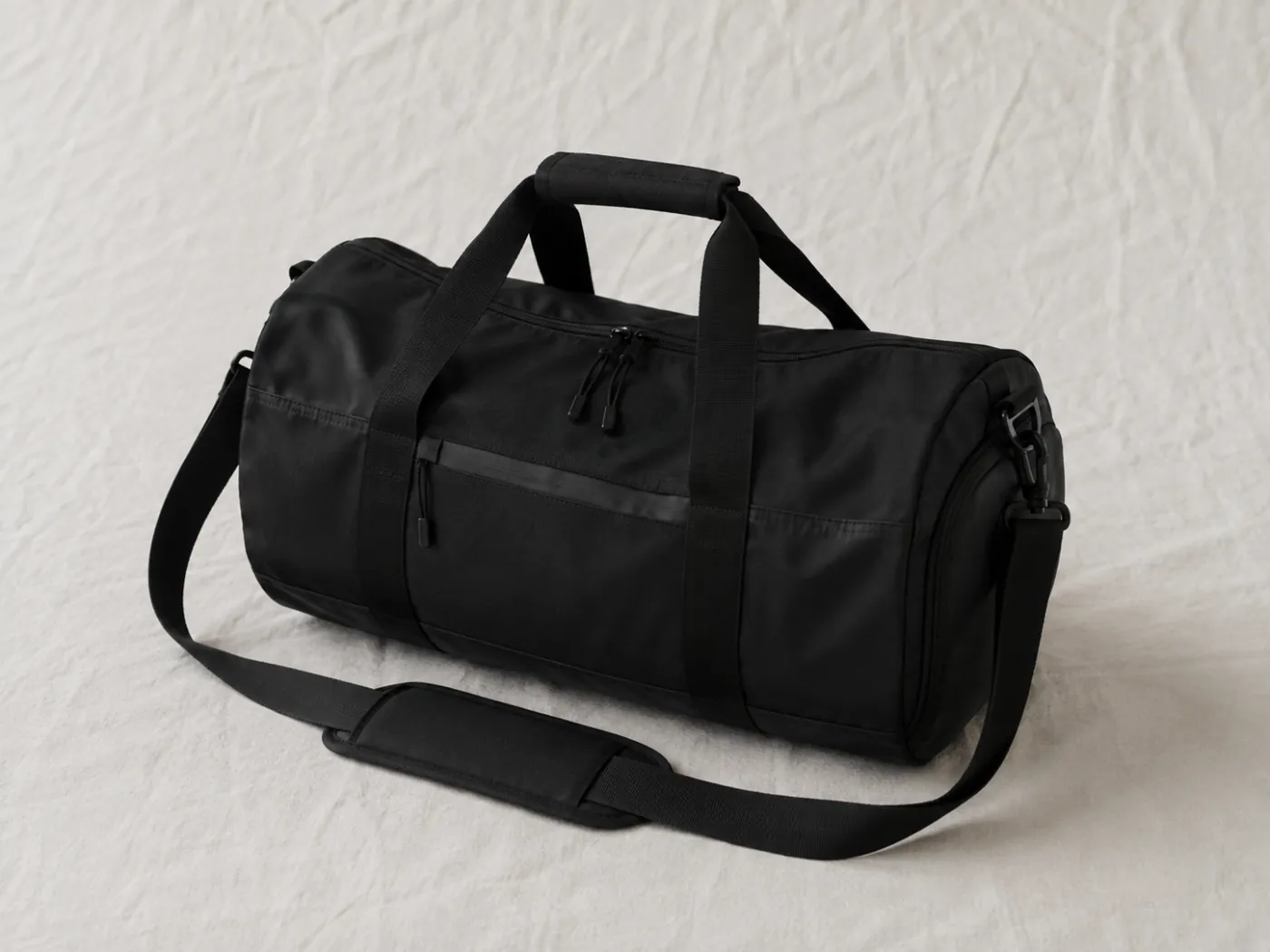 A black weekend duffel bag lying on a pale stone floor.