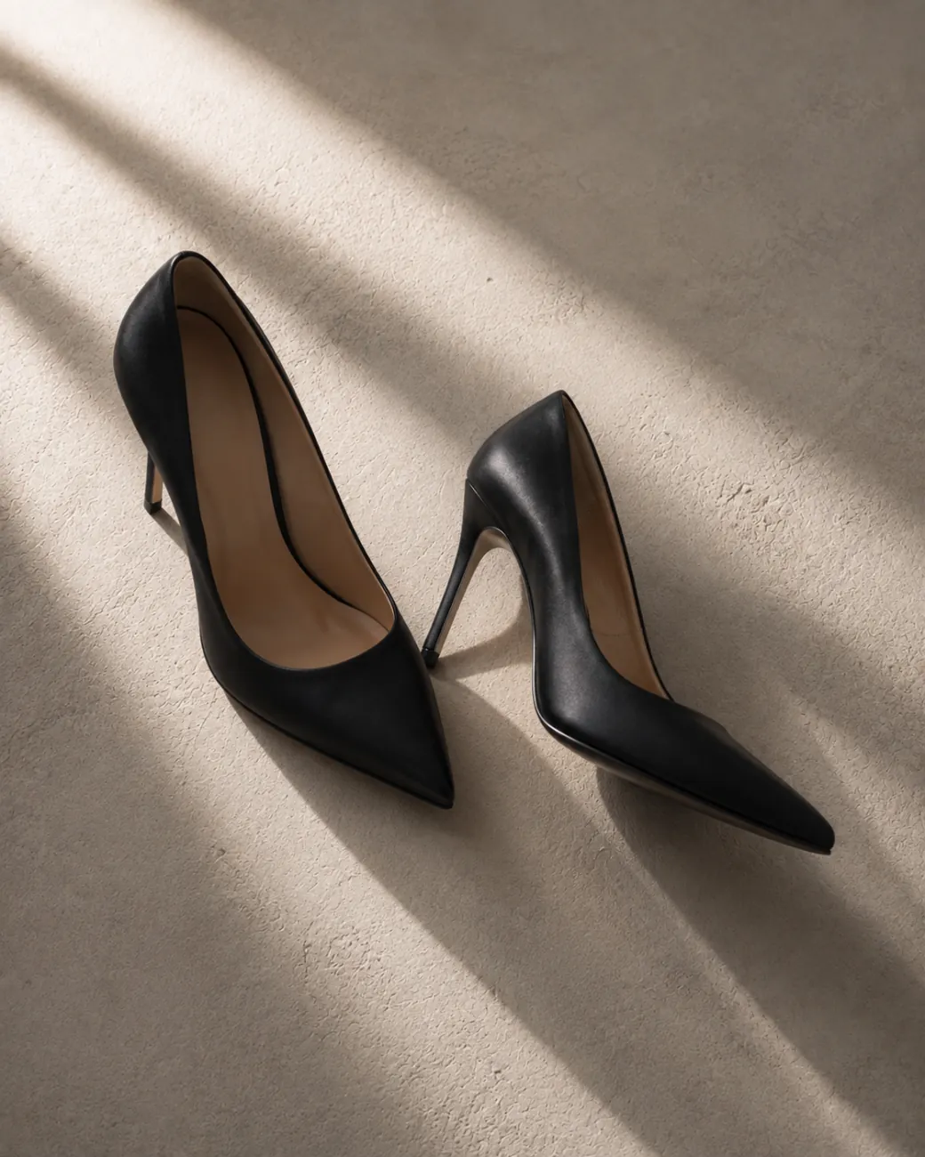 A pair of black heels on stone, in low raking light.