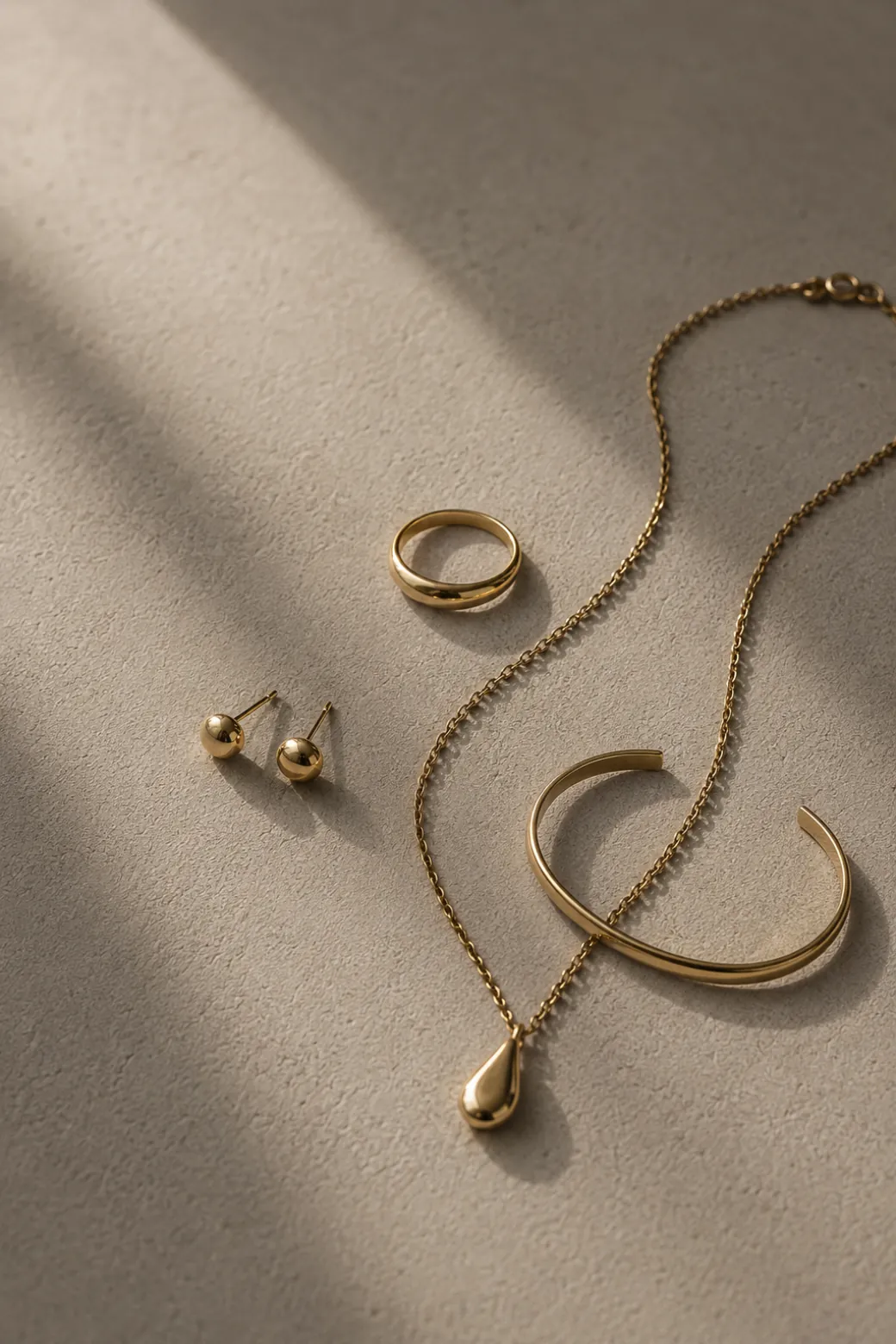 Gold rings and a fine chain on a warm surface, with long shadows.